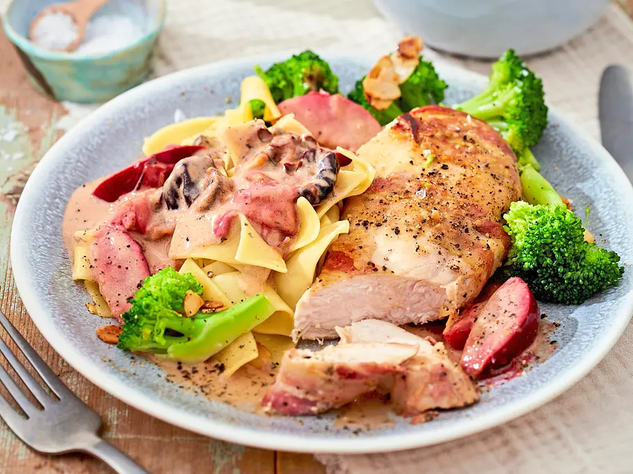 Hähnchenfilet mit Pflaumensoße Auf einem Teller liegen gebratenes Fleisch, Bandnudeln mit cremiger Pilzsoße und Brokkoli. Dahinter steht Brokkoli mit Mandeln.