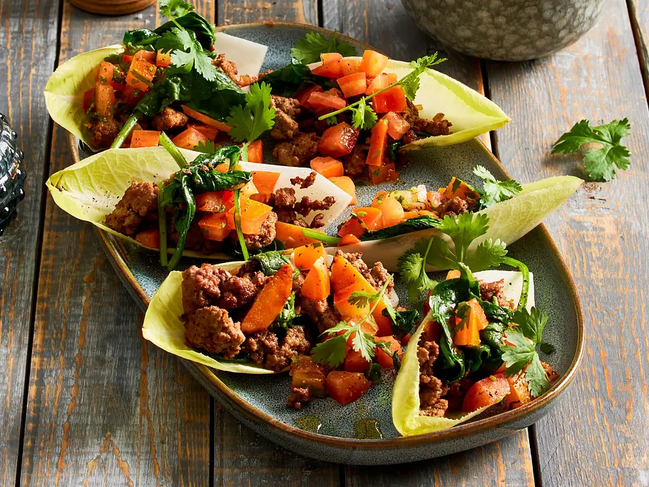 Chicorée-Tacos mit Tomaten-Salsa Gefüllte Chicorée-Blätter mit würzigem Hackfleisch, frischer Tomatensalsa und Koriander angerichtet auf einem länglichen Keramikteller.