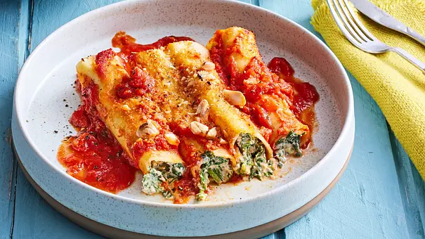 Überbackene Lasagne-Rolls mit Spinat-Ricotta-Füllung in fruchtiger Tomatensauce, mit etwas Käse und gehackten Nüssen bestreut, serviert auf einem hellen Teller. - Foto: LECKER @ Bauer Media Group