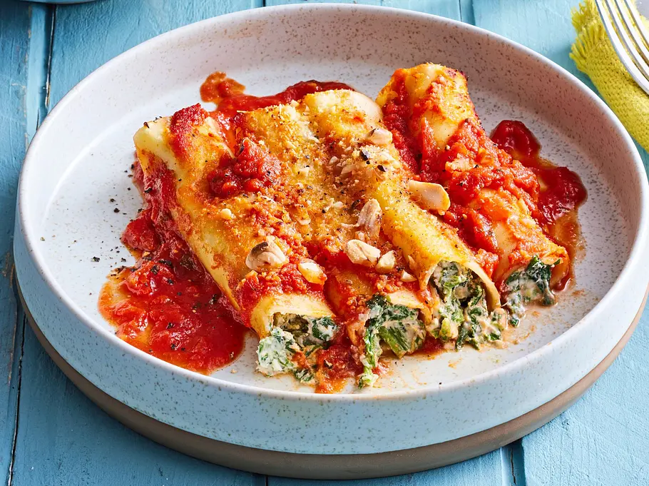 Lasagne-Rolls mit Spinat Rezept Überbackene Lasagne-Rolls mit Spinat-Ricotta-Füllung in fruchtiger Tomatensauce, mit etwas Käse und gehackten Nüssen bestreut, serviert auf einem hellen Teller.