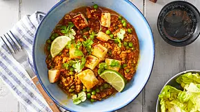 Halloumi-Hack-Pfanne mit würzigem Hackfleisch, grünen Erbsen und goldbraun gebratenen Halloumi-Würfeln, verfeinert mit Koriander und Limettenspalten, serviert in einer Pfanne und in einer blauen Schale mit Holzlöffel. - Foto: LECKER @ Bauer Media Group