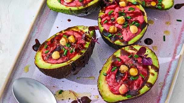Halbierte Avocados, gefüllt mit leuchtend pinkem Rote-Bete-Hummus, garniert mit Kichererbsen, frischen Kräutern und etwas Balsamico, angerichtet auf einer hellen, rechteckigen Servierplatte. Daneben liegen zwei Löffel auf der Platte. - Foto: LECKER @ Bauer Media Group Halbierte Avocados, gefüllt mit leuchtend pinkem Rote-Bete-Hummus, garniert mit Kichererbsen, frischen Kräutern und etwas Balsamico, angerichtet auf einer hellen, rechteckigen Servierplatte. Daneben liegen zwei Löffel auf der Platte. - Foto: LECKER @ Bauer Media Group