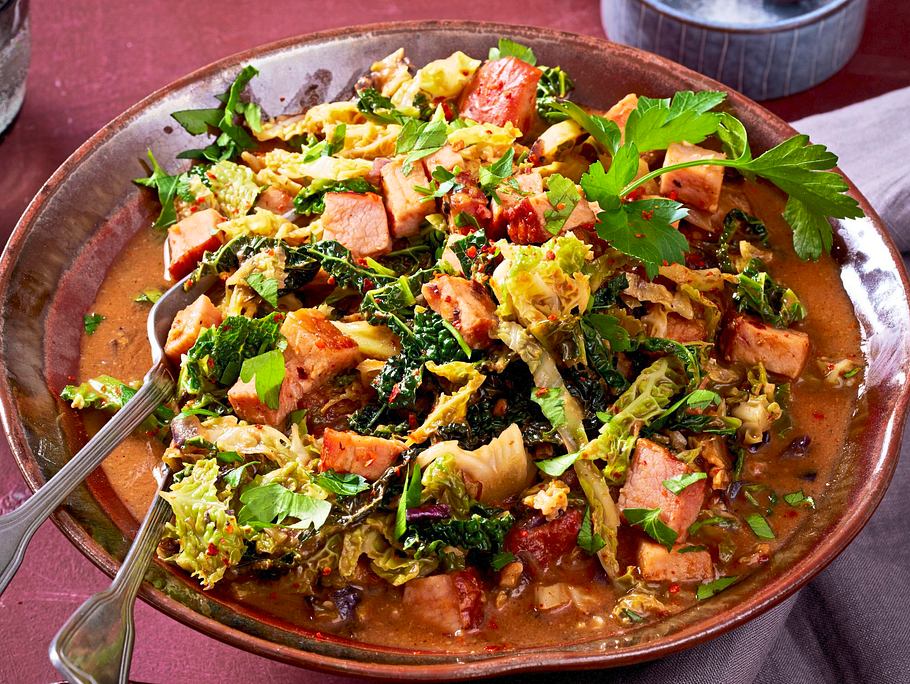 Würziges Ragout mit Kasselerwürfeln, Wirsing, asiatischen Gewürzen und frischen Kräutern, serviert in einer braunen Schale.