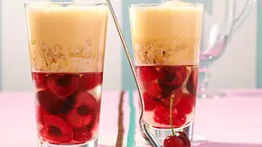Zwei Gläser mit Schichtdessert aus Kirschen, Kirschgelee, zerbröseltem Biskuit und gelber Creme auf einem rosa Tisch, ein langer Löffel und eine Kirsche als Dekoration. - Foto: LECKER @ Bauer Media Group Zwei Gläser mit Schichtdessert aus Kirschen, Kirschgelee, zerbröseltem Biskuit und gelber Creme auf einem rosa Tisch, ein langer Löffel und eine Kirsche als Dekoration. - Foto: LECKER @ Bauer Media Group