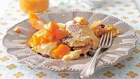 Locker zerzupfter Kaiserschmarrn mit Rosinen, bestäubt mit Puderzucker, auf einem verzierten grauen Teller, dazu leuchtend gelbes Kompott und Gabel. - Foto: LECKER @ Bauer Media Group