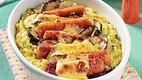 Überbackene Fischstäbchen auf cremigem Kartoffel-Zucchini-Gratin, goldbraun gratiniert und serviert in einer ovalen weißen Auflaufform auf gemusterter Stoffserviette. - Foto: LECKER @ Bauer Media Group