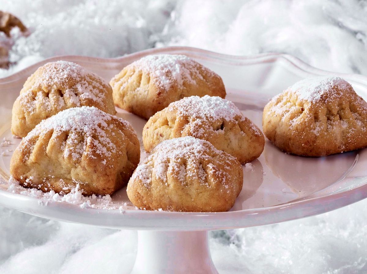 Stollen-Kissen mit Walnussfüllung, bestäubt mit Puderzucker, auf einer Tortenplatte im Schneesetting serviert.