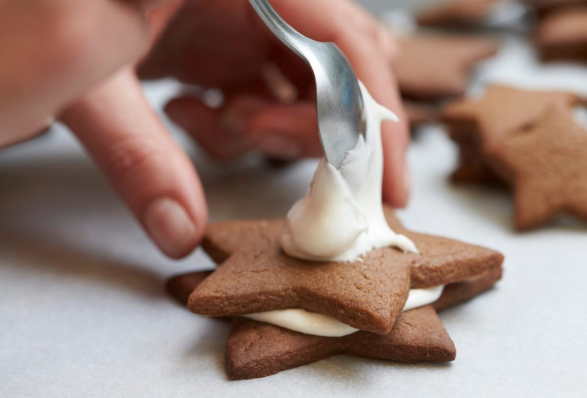 Handgriff Braune Keks-Tannenbäume Hand stapelt sternförmige Kekse mit Zuckerguss zu einem Keks-Tannenbaum.