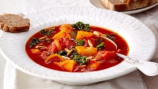 Kräftiger Eintopf mit Süßkartoffeln, Tomaten, Grünkohl und gerösteten Kernen in einem tiefen weißen Teller. - Foto: LECKER @ Bauer Media Group