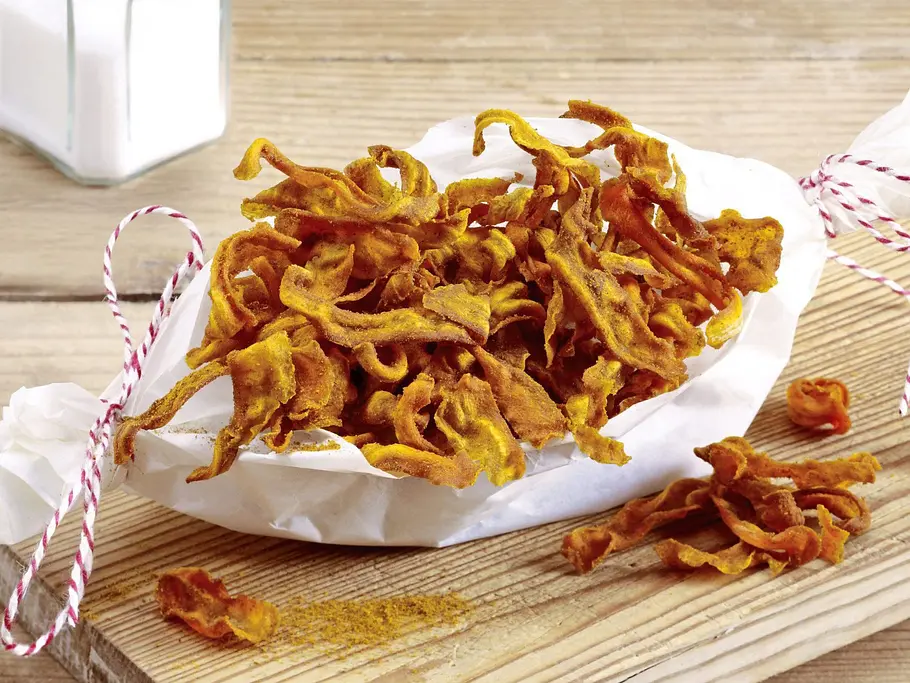 Möhren-Chips Rezept Knusprige Möhren-Chips in Pergamentpapier, serviert auf einem rustikalen Holzbrett.
