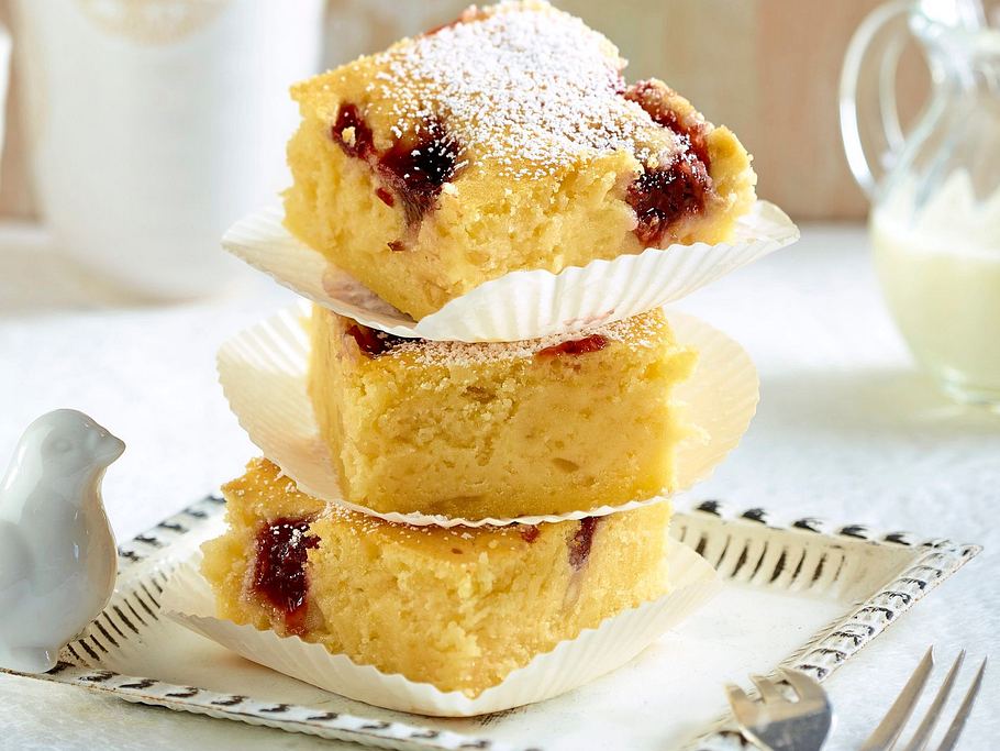 Saftige Macadamia-Blondies mit Vanille, durchzogen von Marmelade, in Würfel geschnitten und mit Puderzucker bestäubt.