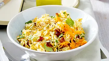Orientalischer Reissalat mit Möhrenraspeln, Kräutern und Sesam in einer weißen Schale, dazu großer Löffel auf heller Serviette. - Foto: LECKER @ Bauer Media Group