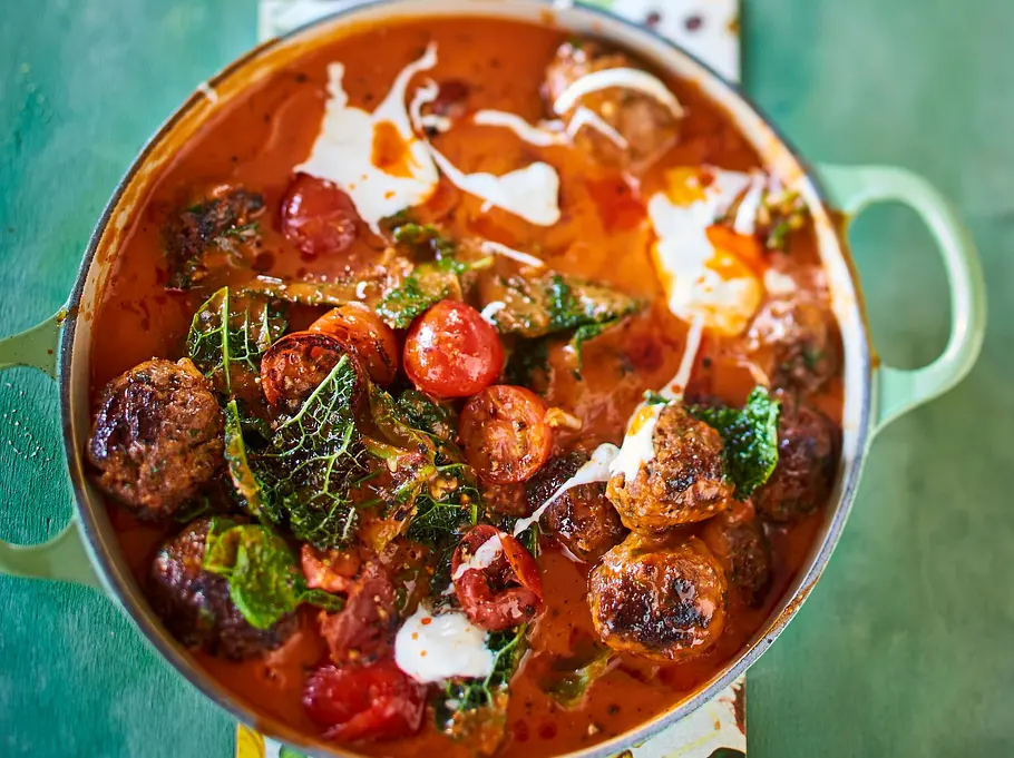Kräftiger Tomaten-Wirsing-Eintopf mit saftigen, gebräunten Meatballs, kombiniert mit frischen Wirsingblättern und einem Klecks Meerrettich, serviert in einem runden, hellgrünen Schmortopf auf gemusterter Unterlage. Die rote, aromatische Sauce und die bunten Zutaten wirken besonders appetitlich.