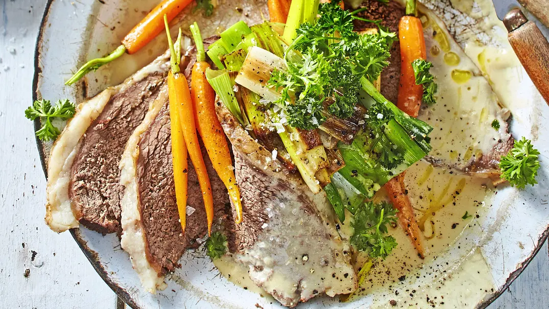 Zarte Scheiben Tafelspitz mit cremiger Meerrettichsoße, dazu glasierte junge Möhren und Lauchstücke, auf einem großen, hellen Teller angerichtet und mit frischer Petersilie bestreut. - Foto: LECKER @ Bauer Media Group