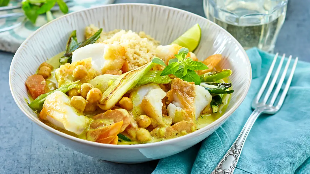 Fischcurry mit Kichererbsen, Lauch und Möhren in einer hellen Schale, dazu lockerer Couscous und frische Minze, angerichtet auf einer blauen Stoffserviette. - Foto: StockFood Studios / Meike Bergmann