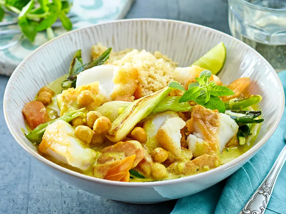 Fischcurry mit Couscous Rezept Fischcurry mit Kichererbsen, Lauch und Möhren in einer hellen Schale, dazu lockerer Couscous und frische Minze, angerichtet auf einer blauen Stoffserviette.