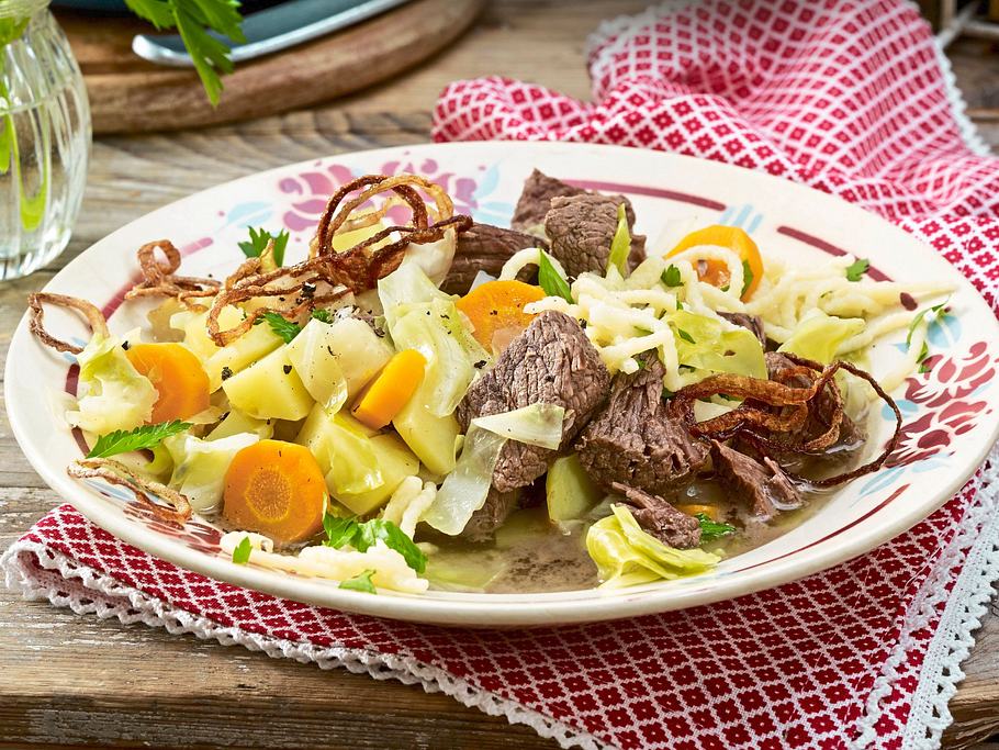 Herzhafter Eintopf aus Rindfleisch, Kartoffeln, Karotten, Filderkraut und Spätzle, serviert auf einem bunten Teller und mit Röstzwiebeln garniert.