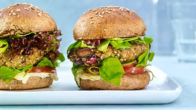Zwei Grünkern-Burger mit Vollkornbrötchen, Salat, Tomaten, frischen Kräutern und cremigem Dip, auf einer rechteckigen weißen Platte. - Foto: LECKER @ Bauer Media Group
