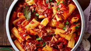Rigatoni-Nudeln in leuchtend roter Tomatensoße mit Pancetta, garniert mit Petersilie, serviert in einer weißen Keramikschüssel auf einem rustikalen Holztisch. - Foto: LECKER @ Bauer Media Group