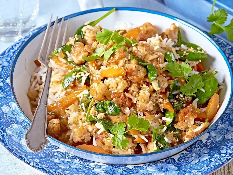 Gebratene Asia-Pfanne mit Putenhackfleisch, Reis, Gemüse und frischem Koriander in einer weißen Schale, serviert auf einem blau-gemusterten Teller.