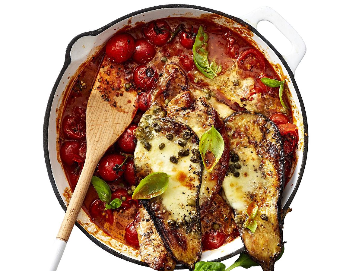 Überbackene Schnitzel-Auberginen in Doppeldecker-Optik auf Tomatensugo mit frischen Kirschtomaten und Basilikum, serviert in einer Auflaufform.