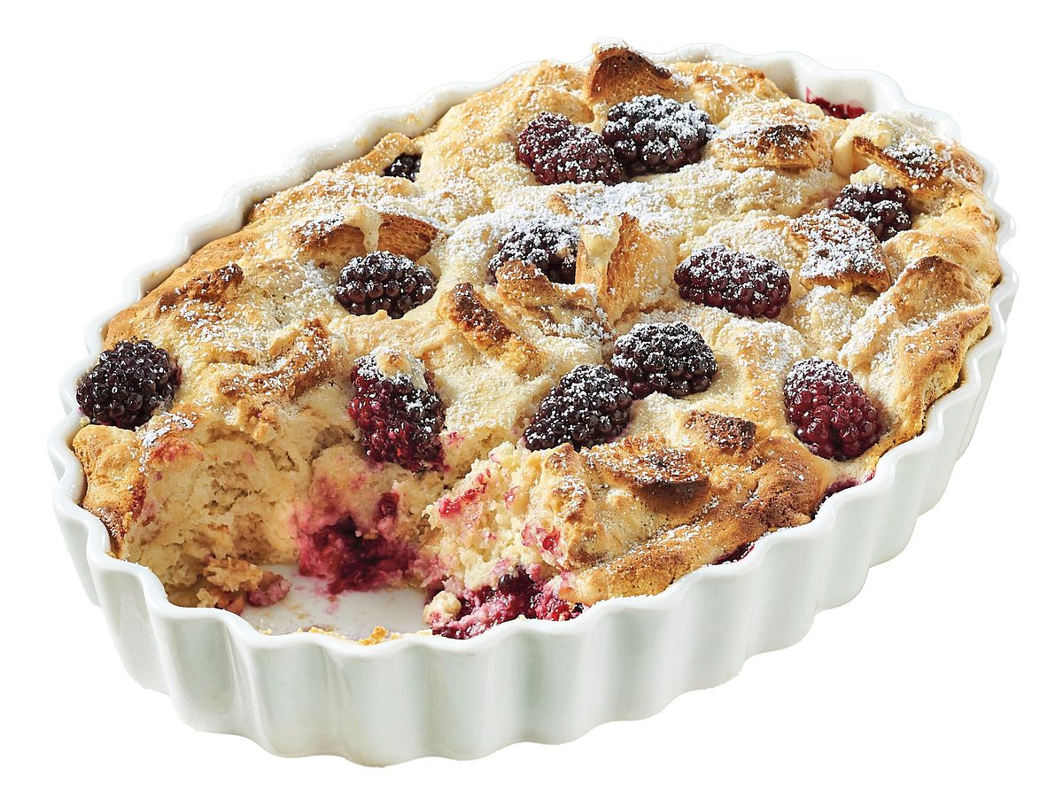 Süßer Quarkauflauf mit Brombeeren und Puderzucker in einer weißen Auflaufform.