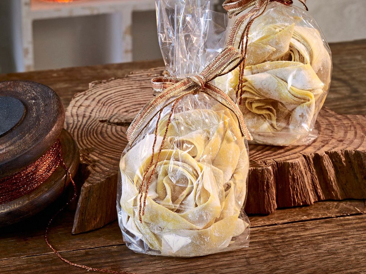 Hausgemachte Safran-Nudeln zu dekorativen Nestern geformt, in durchsichtigen Tütchen mit Schleife verpackt, auf einem rustikalen Holztisch angerichtet.