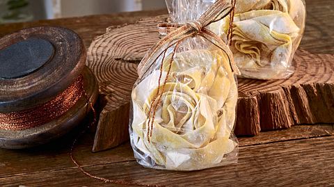 Hausgemachte Safran-Nudeln zu dekorativen Nestern geformt, in durchsichtigen Tütchen mit Schleife verpackt, auf einem rustikalen Holztisch angerichtet. - Foto: LECKER @ Bauer Media Group