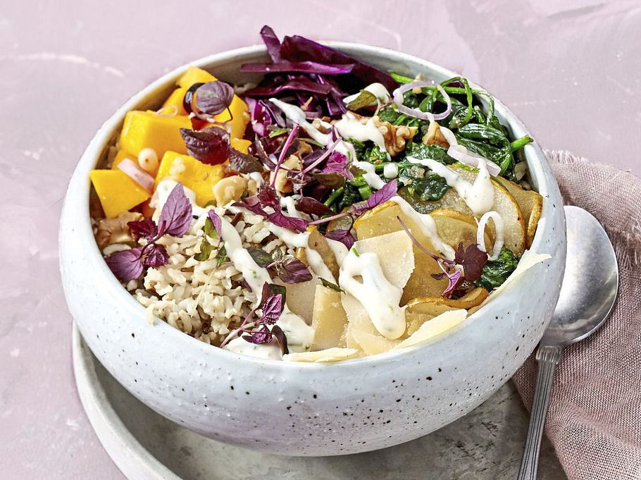 Bunte Bowl mit Reis, frischer Mango, Birnenscheiben, Blattspinat, Rotkohl und Kräutern, getoppt mit einem hellen Dressing, serviert in einer hellen Schale auf einem passenden Teller.