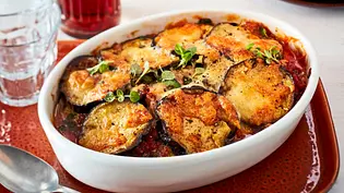 Überbackenes Auberginen-Linsen-Gratin in einer weißen Auflaufform auf einem roten Teller, mit goldbrauner Käseschicht und frischen Kräutern bestreut. Daneben ein silberner Löffel. - Foto: LECKER @ Bauer Media Group Überbackenes Auberginen-Linsen-Gratin in einer weißen Auflaufform auf einem roten Teller, mit goldbrauner Käseschicht und frischen Kräutern bestreut. Daneben ein silberner Löffel. - Foto: LECKER @ Bauer Media Group