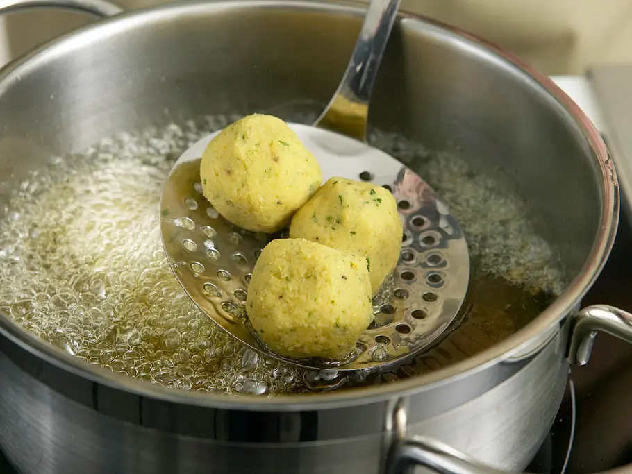 Drei geformte Falafelbällchen werden mit einer Schaumkelle in das Frittieröl gehoben.