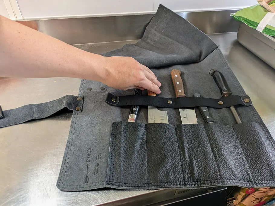 Eine geöffnete F. Dick Messertasche mit mehreren Messern liegt auf einer Arbeitsfläche, eine Hand greift nach einem Messer.