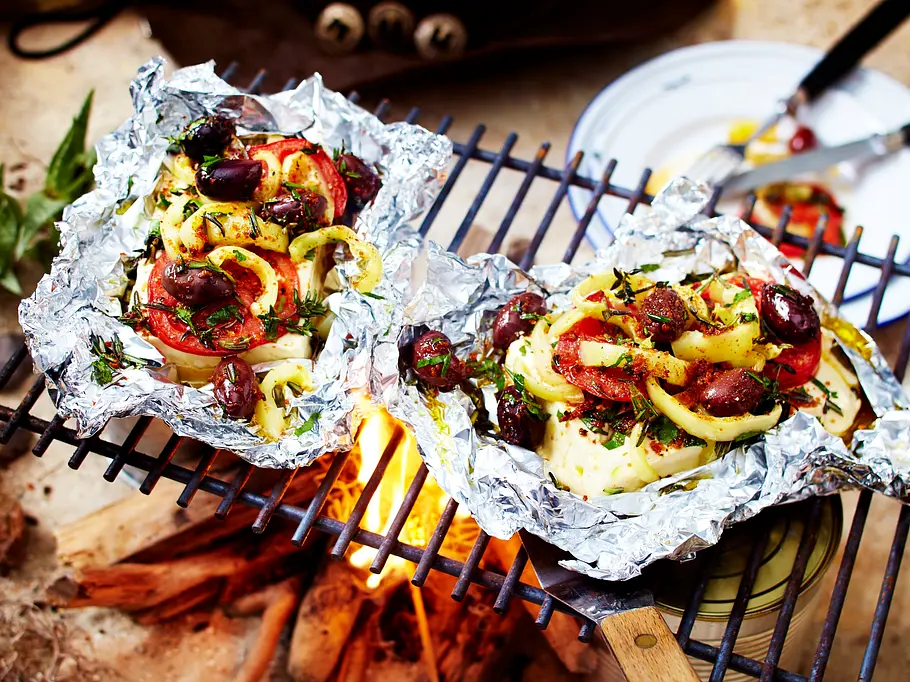 Gegrillte Feta-Päckchen mit Oliven, Paprika und Tomaten in Alufolie auf dem Grillrost