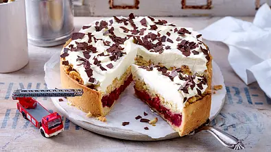 Ein angeschnittener Feuerwehrkuchen auf einem Tortenteller, an der Seite ein Spielzeug-Feuerwehrauto. - Foto: LECKER @ Bauer Media Group