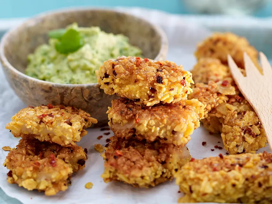 8 knusprige Hähnchen-Nuggets mit Holzgabel und einer Schale Guacamole.