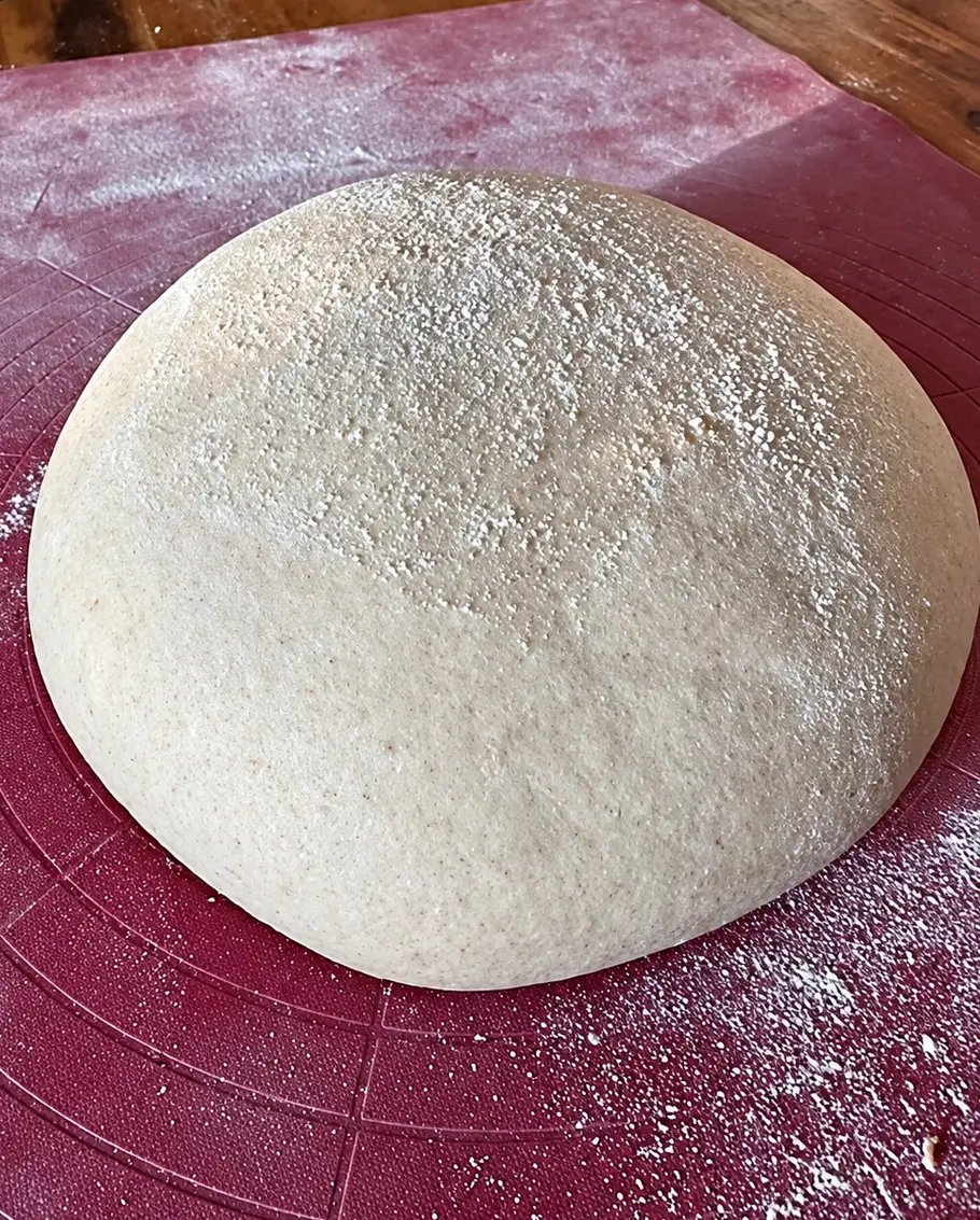 Finales gehen, pre-shape Ein runder, mit Mehl bestäubter Teig liegt auf einer rosafarbenen Backmatte mit Kreislinien auf einem Holztisch.