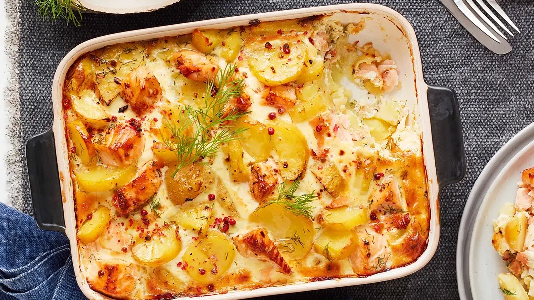 Finnischer Lachsauflauf mit goldgelben Kartoffelscheiben, zarten Lachsstücken und Dill, in einer rechteckigen Auflaufform auf einer strukturierten, dunklen Unterlage serviert. - Foto: LECKER @ Bauer Media Group Finnischer Lachsauflauf mit goldgelben Kartoffelscheiben, zarten Lachsstücken und Dill, in einer rechteckigen Auflaufform auf einer strukturierten, dunklen Unterlage serviert. - Foto: LECKER @ Bauer Media Group