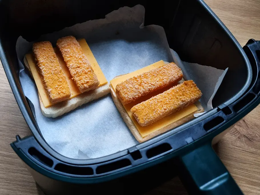 Fischstäbchen-Toast Airfryer Fischstäbchen-Toasts liegen auf Backpapier im Garkorb des Airfryers.