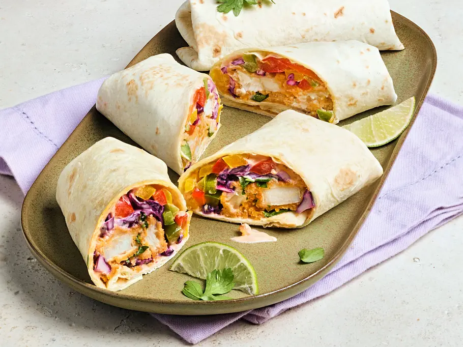 Vier Stücke Fischstäbchen-Wraps, gefüllt mit knusprigen Fischstäbchen, buntem Gemüse und Soße, angerichtet auf einem ovalen, grünen Teller mit etwas Limette und frischer Petersilie als Dekoration.