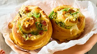 Zwei Laugenschnecken mit Käse-Schinken-Ziebel-Füllung liegen auf einem rosa Teller, sie sind goldbraun gebacken - Foto: LECKER @ Bauer Media Group