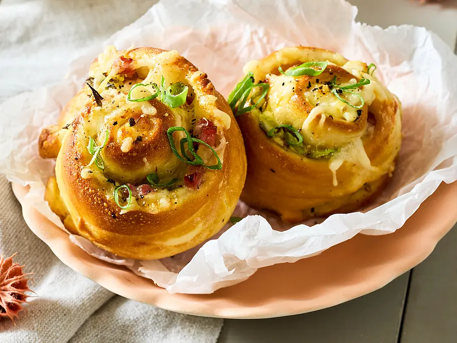 Zwei Laugenschnecken mit Käse-Schinken-Ziebel-Füllung liegen auf einem rosa Teller, sie sind goldbraun gebacken