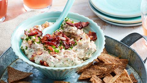 Ein hellblaues Schälchen gefüllt mit Flammkuchen-Dip, das auf einem Zinktablett mit Kräckern steht. - Foto: House of Food / Bauer Food Experts KG