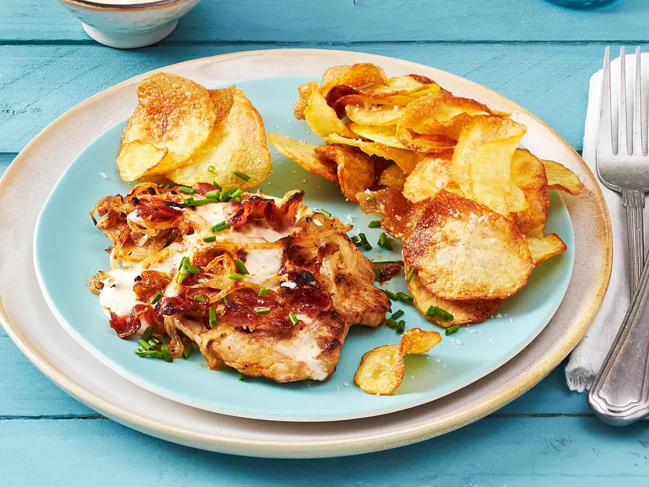 Knuspriges Flammkuchen-Schnitzel aus dem Airfryer, belegt mit Schmand, Zwiebeln und Speckwürfeln, serviert mit hausgemachten Kartoffelchips auf einem hellblauen Teller. Daneben eine Schale Dip.