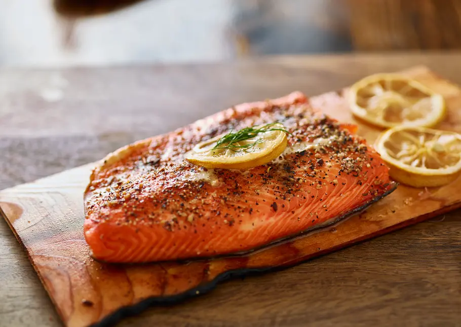 Servierfertiger, mit Kräutern garnierter Flammlachs auf einem Holzbrett