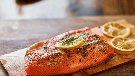 Servierfertiger, mit Kräutern garnierter Flammlachs auf einem Holzbrett - Foto: iStock/rez-art