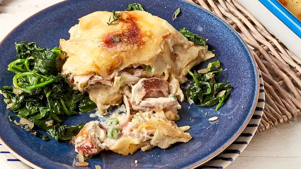 Französischer Crêpes-Auflauf, goldbraun überbacken, gefüllt mit zartem Dijon-Hähnchen und serviert auf einem blauen Teller mit sautiertem Blattspinat. - Foto: LECKER @ Bauer Media Group