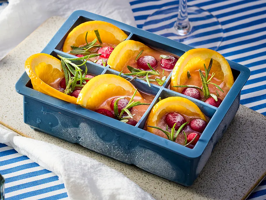 Frozen Weihnachts-Spritz Rezept Eiwürfelform aus Silikon ist mit Grapefruitsaft, Orangenscheiben, Rosmarinzweigen und Cranberrys gefüllt