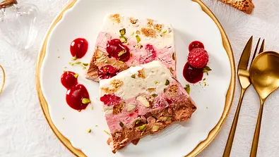 Weihnachtsdessert zum Vorbereiten: Zwei Scheiben Parfait liegen übereinander auf einem kleinen Teller mit Goldrand, drumherum ein paar Kleckse Himbeersoße und eine frische Himbeere  - Foto: LECKER @ Bauer Media Group