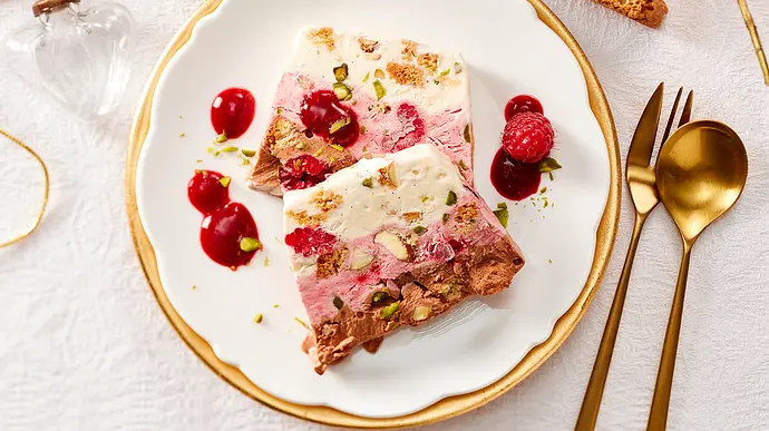 Zwei Scheiben Parfait liegen übereinander auf einem kleinen Teller mit Goldrand, drumherum ein paar Kleckse Himbeersoße und eine frische Himbeere  - Foto: LECKER @ Bauer Media Group