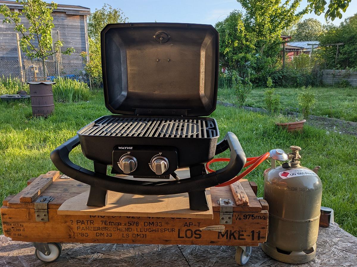 Gasgrill mit Gasflasche daneben im Garten.